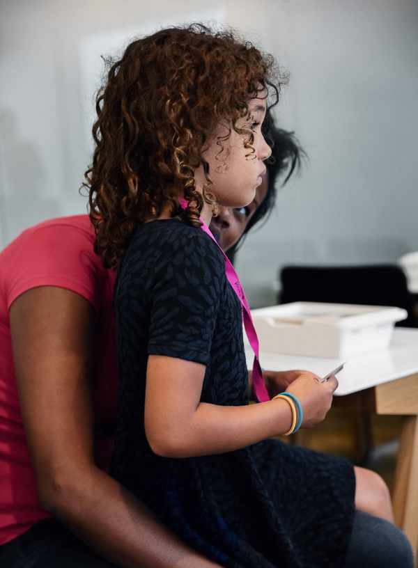 A studious child sits on a woman's lap.